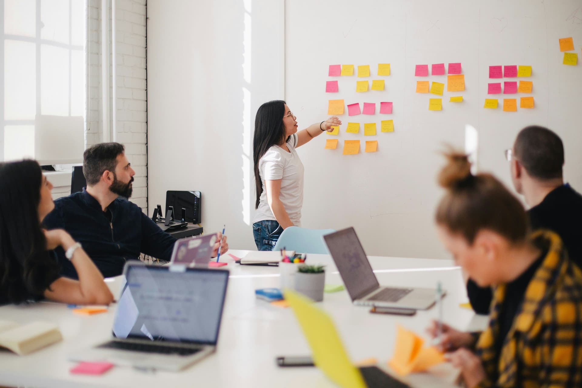 Person pointing at sticky notes on a wall during a meeting.