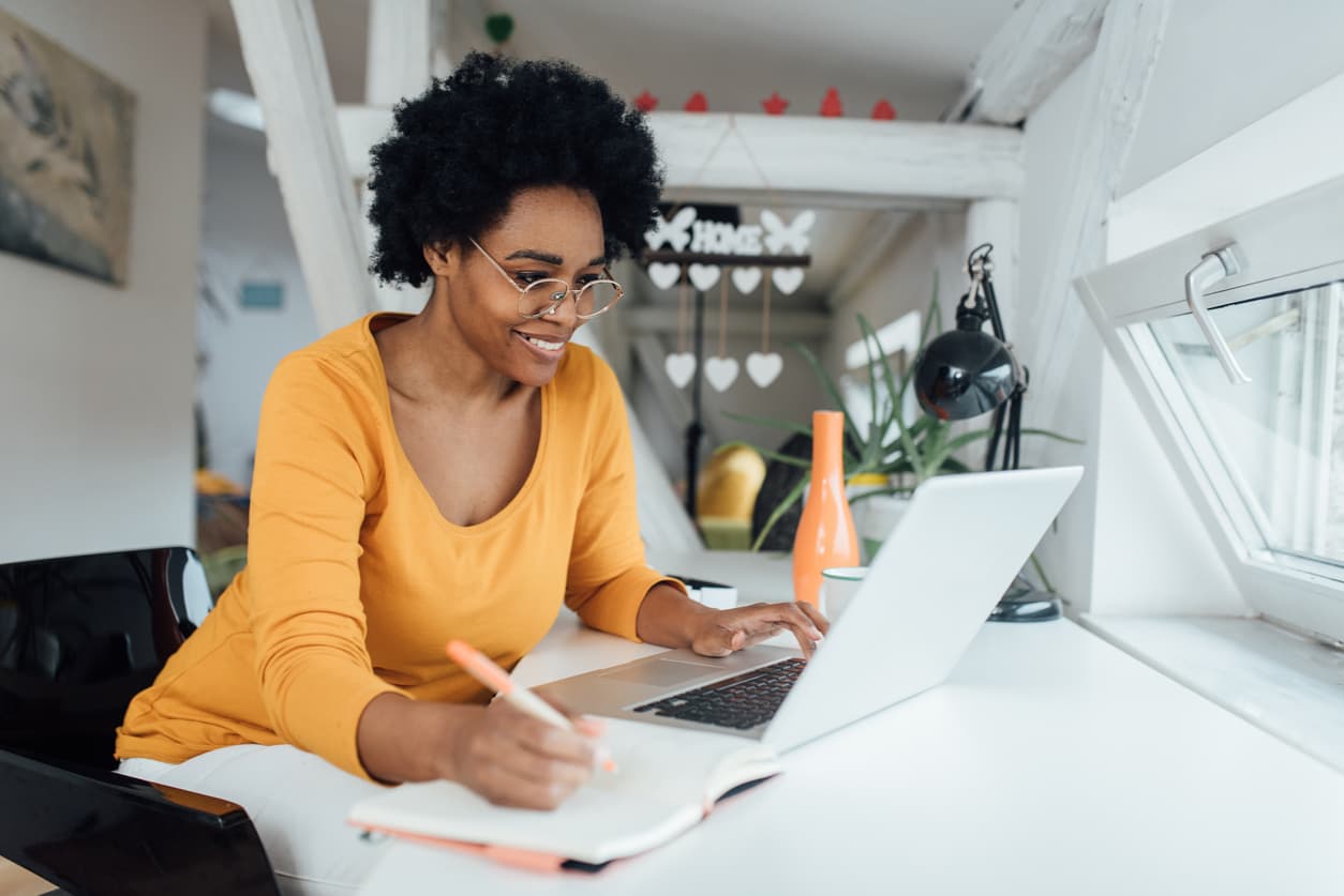 A woman in an orange shirt is focused on her laptop while working at a desk.