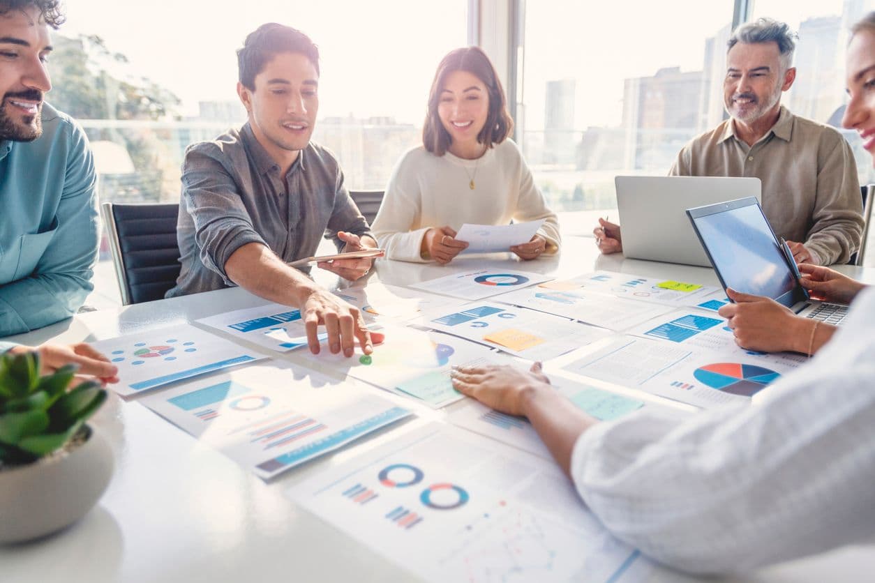 Business people and a college student engage in teamwork at a table, sharing insights and working on a project together.