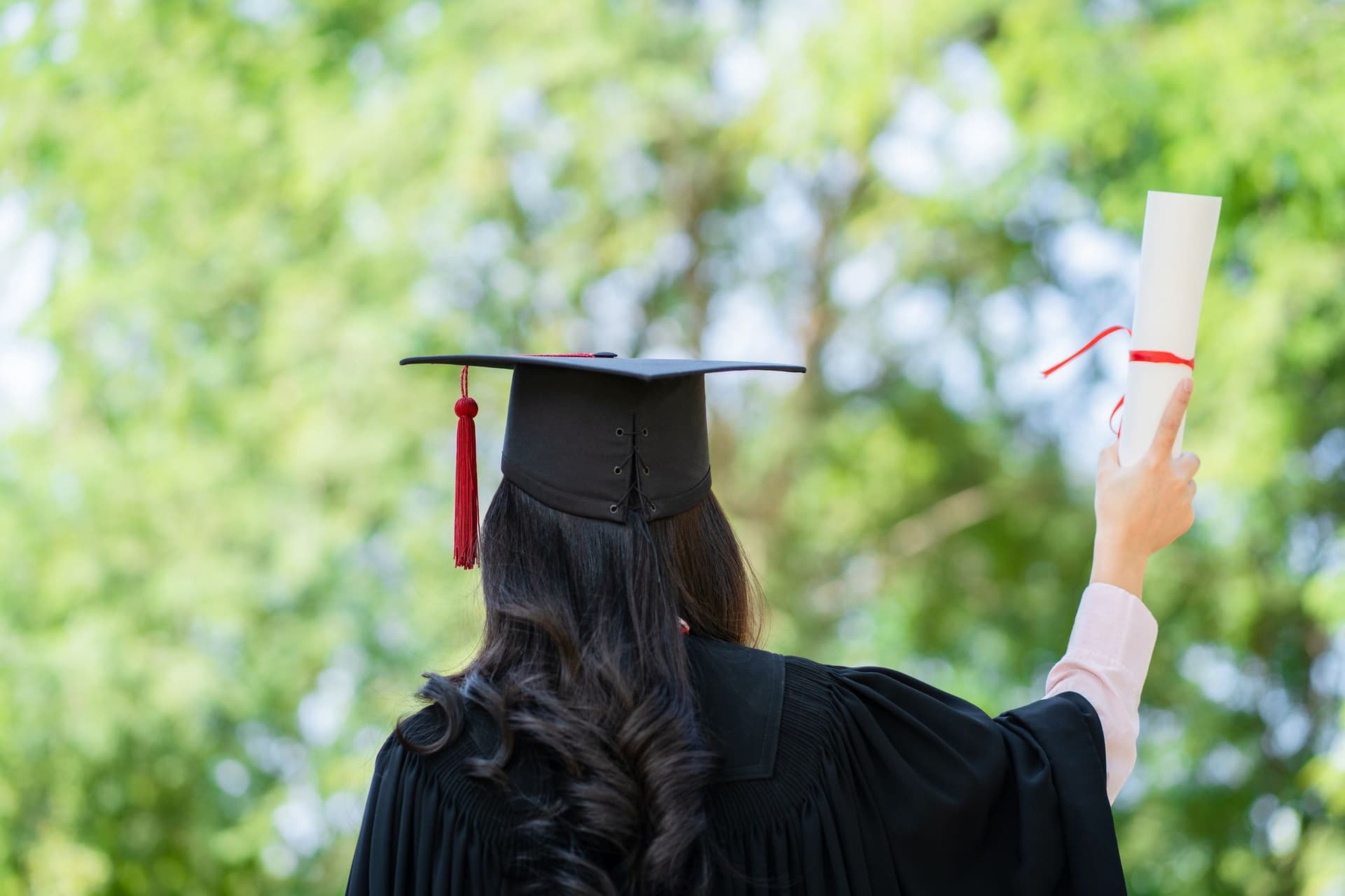 A woman in a graduation gown proudly holds up her diploma, celebrating her academic achievement. 