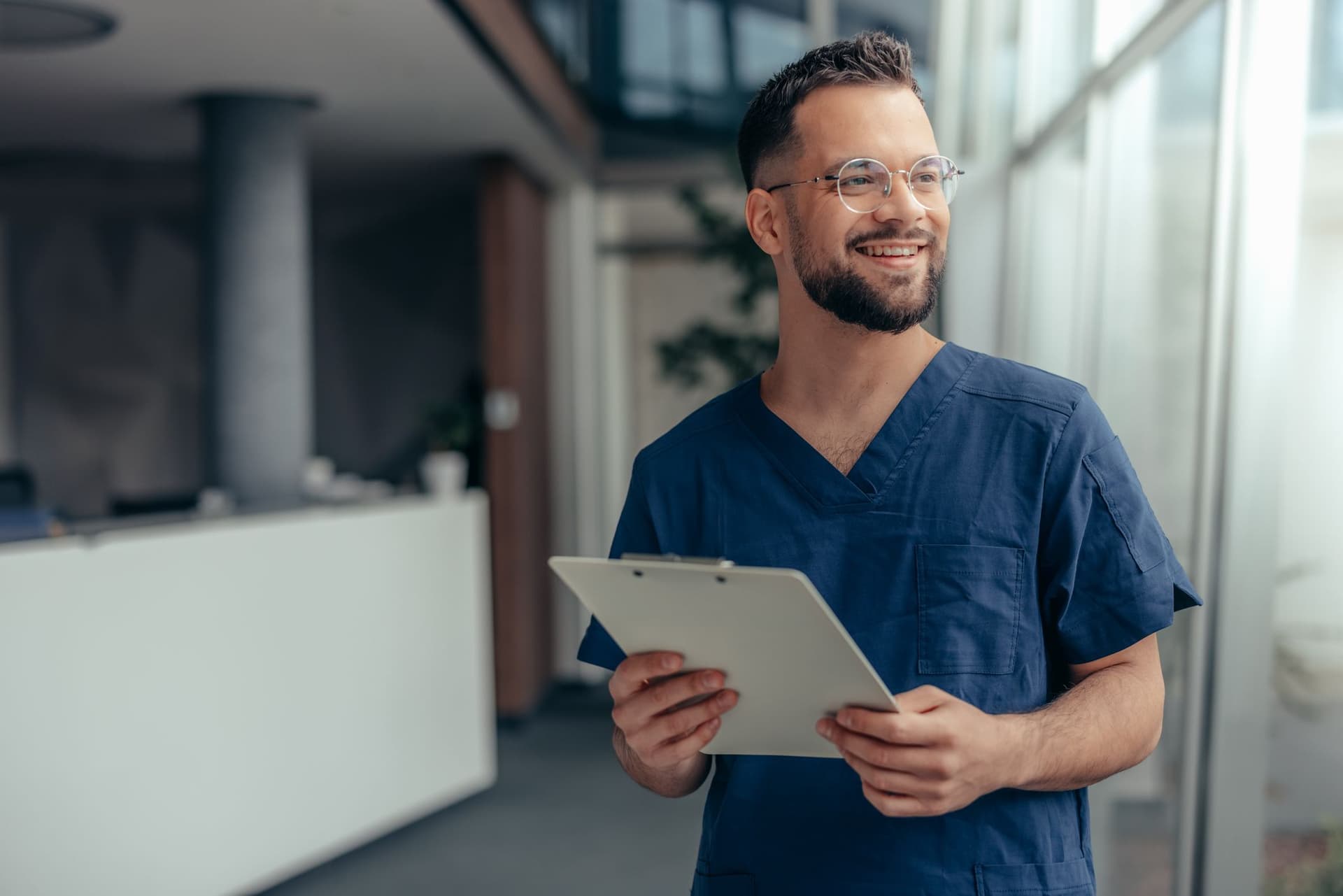 A friendly male doctor smiles while holding a clipboard, symbolizing dedication and support in healthcare