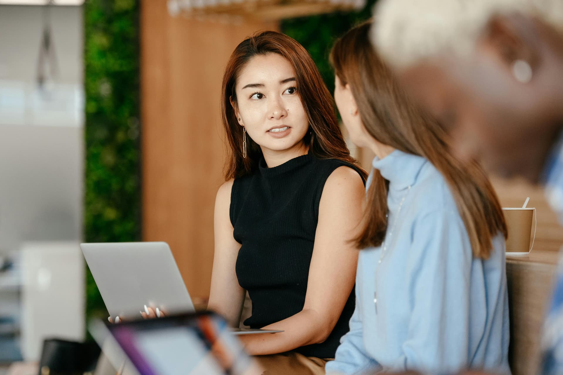 Two people having a conversation, one holding a laptop.